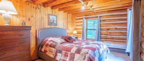 A log cabin bedroom with a bed, dresser, and windows.