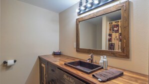 A bathroom with a wooden vanity, a large mirror, and a sink. - Rustic Roost Log Cabin | 1 Bed, 1 Bath (Custer)