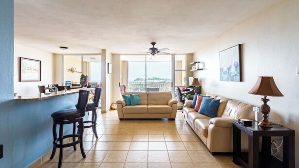 A spacious living area with a kitchen, a dining area, and a balcony with a city view.