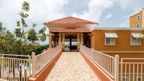 A covered walkway leading to a building with a tiled roof and a balcony.