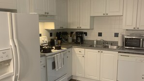 Ett modernt kök med vita skåp, kylskåp, spis, mikrovågsugn och en kaffebryggare.