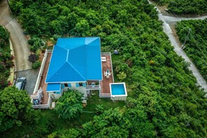 Une grande maison avec un toit bleu, entourée d’une végétation luxuriante.
