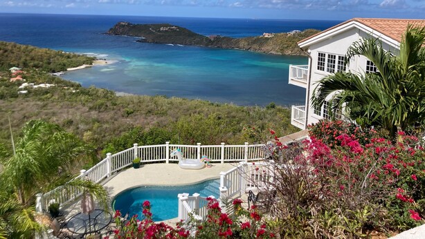 Ein weißes, zweistöckiges Haus mit Balkon, das auf einen Pool und den Küstenblick blickt.