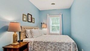 A bedroom with a bed, nightstand, lamp, and framed pictures on the wall. - Secluded Woodland Home with Trail and Lake Access (Pullman)