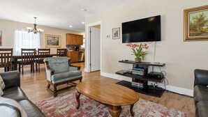 A living room with a TV, a coffee table, a sofa, and a dining area with chairs and a table. - Secluded Woodland Home with Trail and Lake Access (Pullman)