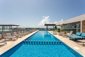 Una piscina infinita en la azotea con sillones de descanso y barandilla de cristal.