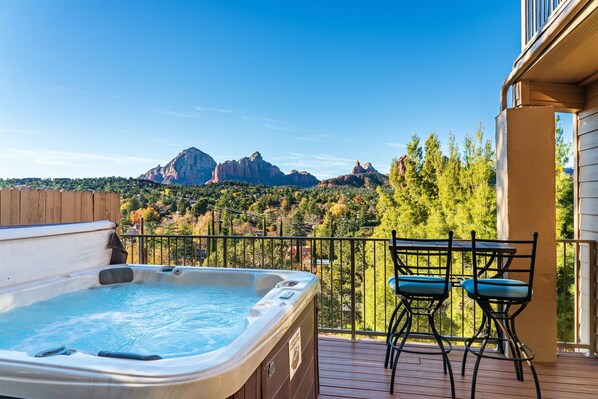Un bain à remous sur une terrasse en bois, avec vue sur les montagnes et les arbres.