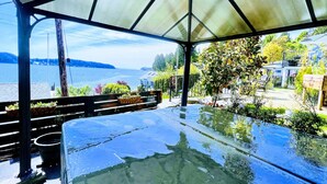 A covered outdoor area with a view of a lake and a house in the background. - Bill's Landing Luxury Suite with private Hot Tub (Gibsons)