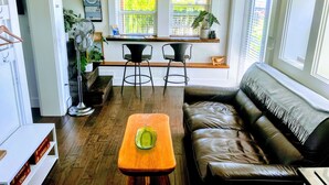 A cozy living room with a leather sofa, a wooden coffee table, and a dining area with a kitchen counter and two chairs. - Bill's Landing Luxury Suite with private Hot Tub (Gibsons)