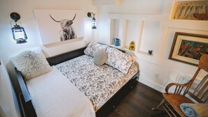 A cozy bedroom with a bed, a chair, and a wall-mounted shelf with decorative items. - Bill's Landing Luxury Suite with private Hot Tub (Gibsons)