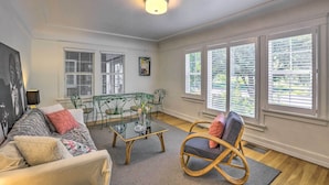 A living room with a sofa, a glass coffee table, a wicker chair, and a dining table with chairs.