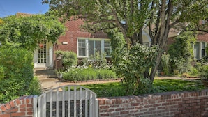 A brick house with a white door, a small front porch, and a brick wall with a white gate.