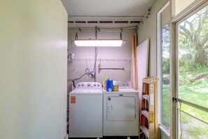 Ett tvättrum med tvättmaskin, torktumlare och ett fönster med utsikt över grönområden.