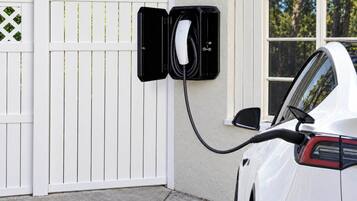Ein weißes Auto steht neben einem weißen Zaun, an dem eine Ladestation angebracht ist.
