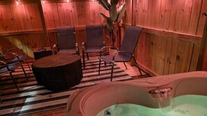 A wooden spa room with a hot tub, seating area, and a potted plant.