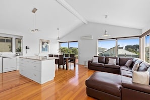 A modern kitchen with white cabinetry, a dining area with a table and chairs, a brown leather sofa, and large windows offering a view.