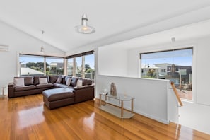 A modern living room with a sectional sofa, a glass coffee table, and large windows offering a view of the neighborhood.