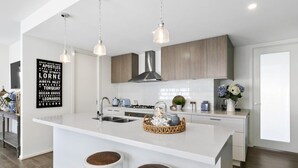 Una cocina moderna con una isla central, luces colgantes, salpicadero y un letrero en la pared.