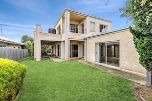 A two-story house with a flat roof, a balcony on the upper floor, and a large sliding glass door on the ground floor. - Cowrie House: Ocean Views, 500m to Fisho’s Beach (Torquay)