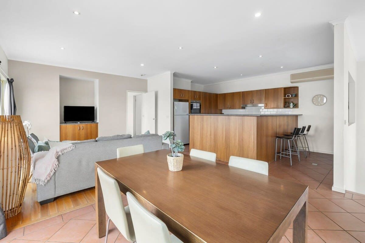 A modern kitchen with wooden cabinets, a built-in oven, and a dining area with a wooden table and white chairs.