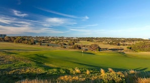 A golf course with a flag, trees, and distant buildings. - Cowrie House: Ocean Views, 500m to Fisho’s Beach (Torquay)