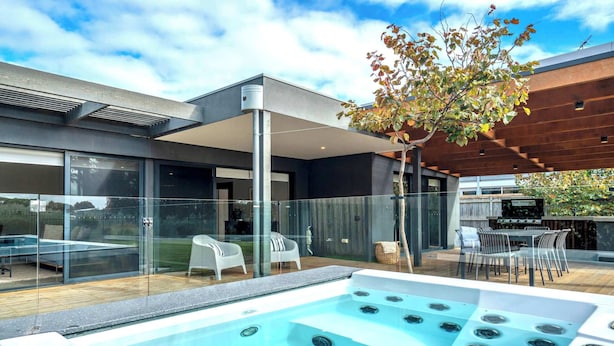 A modern outdoor pool area with a hot tub, glass walls, and a wooden pergola. - Ultimate Luxury family  Home With Spa Pool (Torquay)