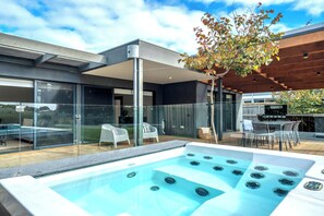 A modern outdoor pool area with a hot tub, glass walls, and a wooden pergola. - Ultimate Luxury family  Home With Spa Pool (Torquay)