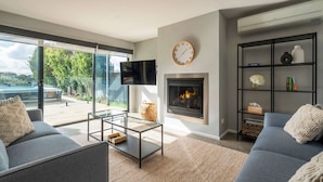 A modern living room with a fireplace, a flat-screen TV, and a glass door leading to a balcony. - Ultimate Luxury family  Home With Spa Pool (Torquay)