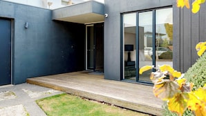 A modern building with a wooden deck, large sliding glass doors, and a visible garage. - Ultimate Luxury family  Home With Spa Pool (Torquay)