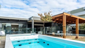 A modern outdoor swimming pool with hot tubs, glass walls, and outdoor seating. - Ultimate Luxury family  Home With Spa Pool (Torquay)