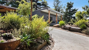 A modern house with a covered porch, surrounded by various plants and trees.