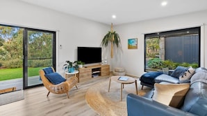 A modern living room with a large TV, comfortable seating, a coffee table, and a view of the outdoors.