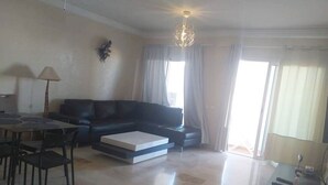A modern living room with a black leather sofa, a dining table with chairs, a coffee table, and a chandelier.