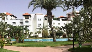 A residential building with multiple balconies, a swimming pool, and a well-maintained garden with palm trees.