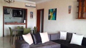 A living room with a grey sofa, a dining table with chairs, and a kitchen area in the background.