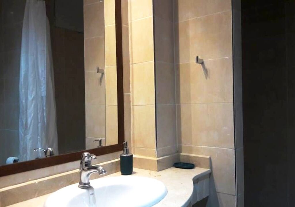 A bathroom with a sink, mirror, and shower area.