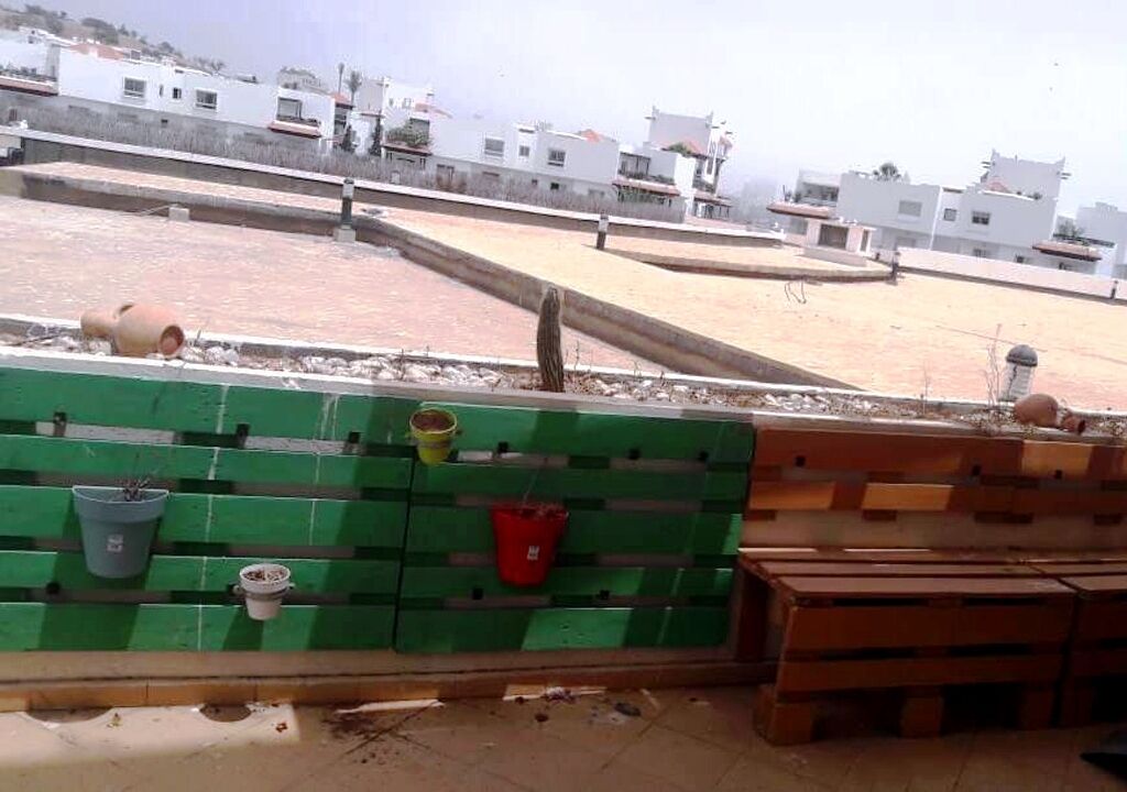 A rooftop terrace with a green partition, potted plants, and wooden benches.