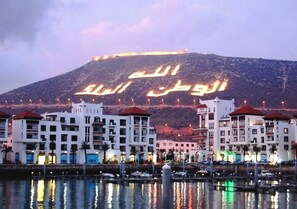 A coastal town with buildings along the waterfront and Arabic script illuminated on a hill in the background. - Marina Agadir Residence 5419 (Agadir)