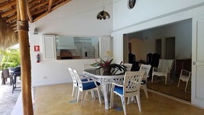A dining area with a round table and white chairs, a kitchen in the background, and a large mirror reflecting the room. - Charmant Bungalow Tropical (Las Terrenas)