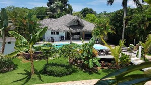 A house with a thatched roof, a swimming pool, and lush tropical vegetation. - Charmant Bungalow Tropical (Las Terrenas)