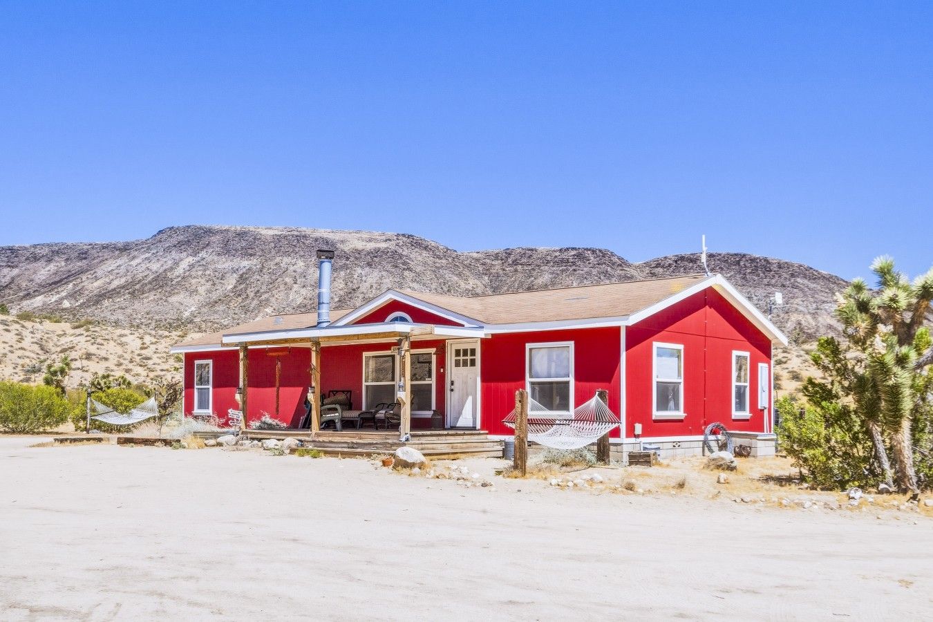 Un edificio rojo con un porche, una chimenea y un paisaje desértico al fondo.