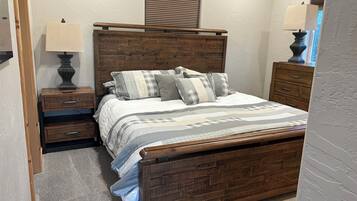 Une chambre à coucher avec une tête de lit en bois, un lit avec une literie à rayures, deux tables de chevet avec des lampes et une commode.
