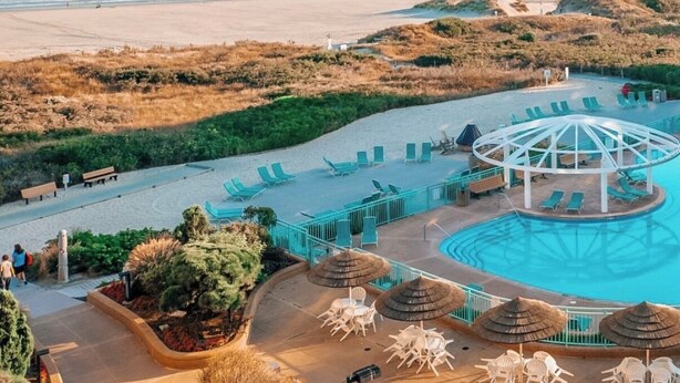 Un complex turístic a la vora de la platja, amb piscina, gandules i un cobert.
