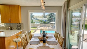 Comedor con mesa de madera, sillas y vista a un patio trasero con piscina y mobiliario exterior.