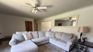 A living room with a sectional sofa, a patterned rug, a ceiling fan, a lamp, and a mirror on the wall. - Pet-Friendly 2BR Near BYU-I with Fenced Yard (Rexburg)