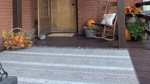 A brick building with a wooden door, a welcome sign, a rocking chair, and a rug on the porch. - Pet-Friendly 2BR Near BYU-I with Fenced Yard (Rexburg)