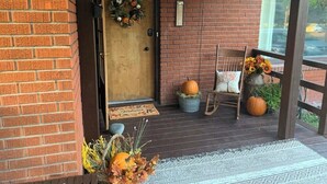 A brick porch with a wooden door, a welcome sign, a chair, a table, and a large pumpkin. - Pet-Friendly 2BR Near BYU-I with Fenced Yard (Rexburg)