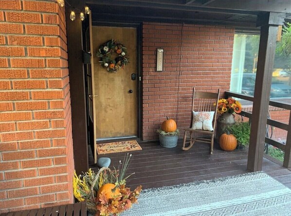 A brick porch with a wooden door, a welcome sign, a chair, a table, and a large pumpkin. - Pet-Friendly 2BR Near BYU-I with Fenced Yard (Rexburg)