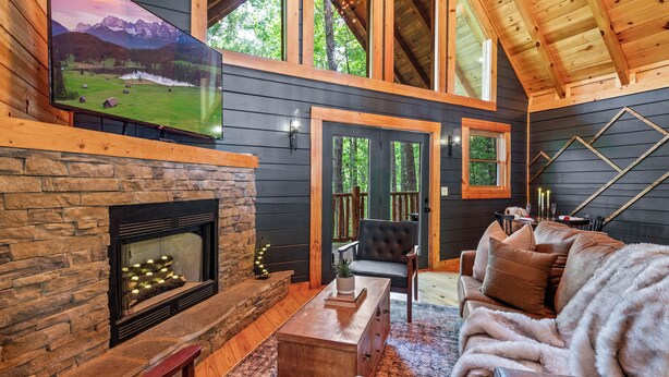 Una sala de estar acogedora con una chimenea de piedra, un televisor de pantalla grande y una zona de estar cómoda con un sofá de cuero y un sillón.