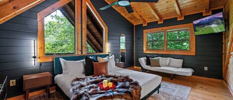 A cozy bedroom with a large bed, a ceiling fan, and a TV mounted on the wall.